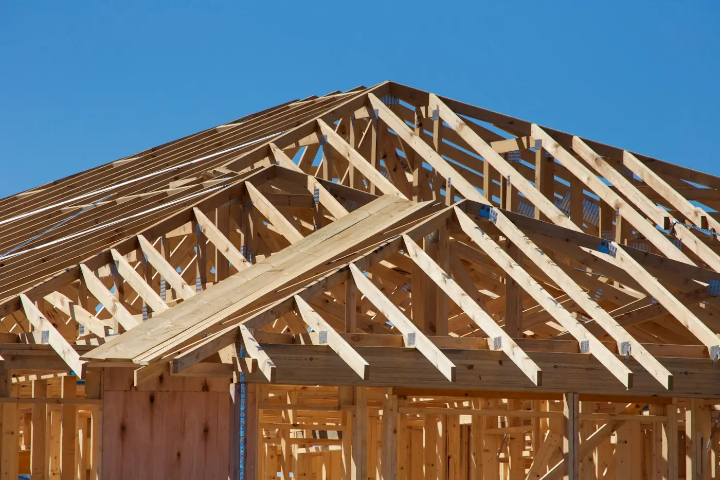 The timber roof trusses of a house under construction, against a blue sky