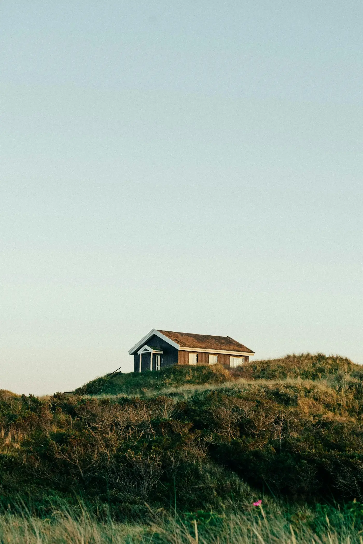 A small house alone on top of a grassy hill under a clear sky